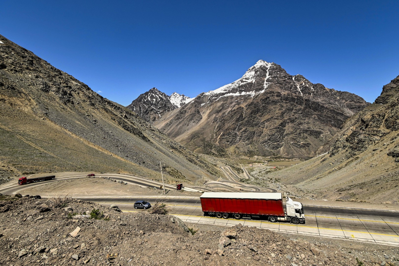 A imagem mostra caminhões em uma estrada de curvas nos Andes.